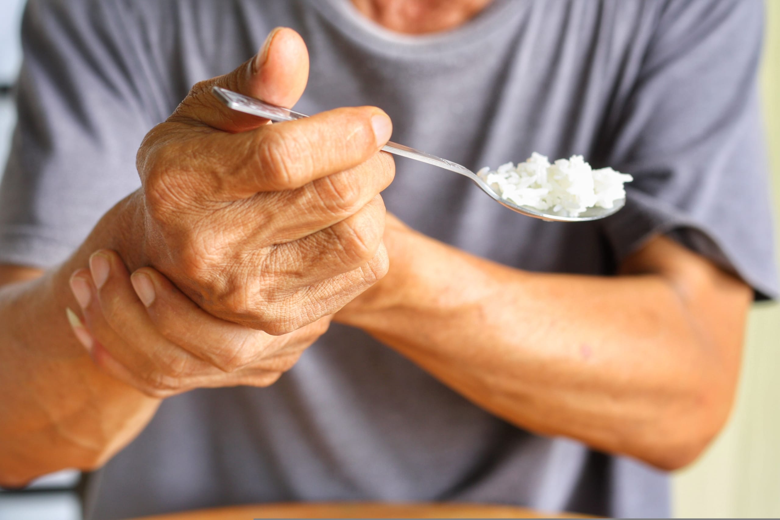Elderly,man,is,holding,his,hand,while,eating,because,parkinson's